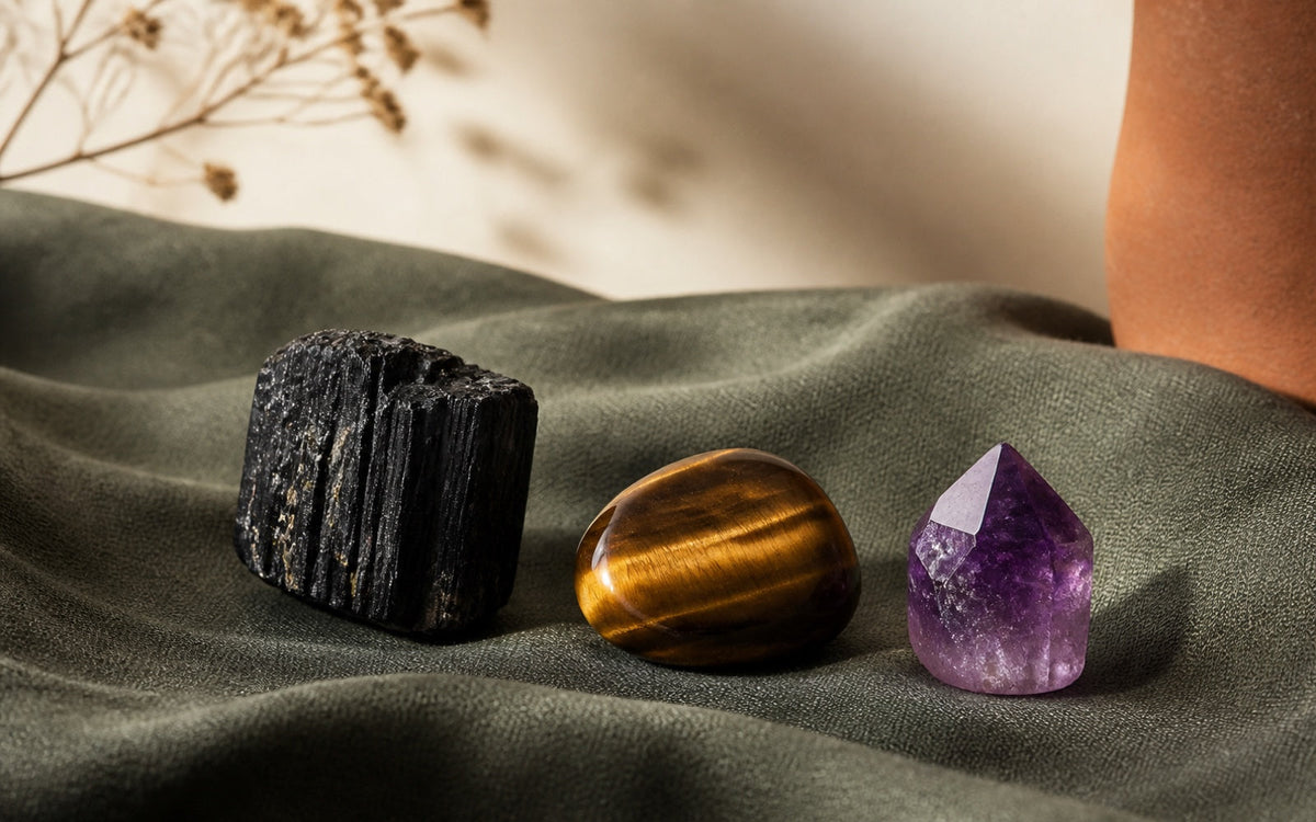 Black tourmaline, a tigers eye stone and an amethyst grouped on dark green linen