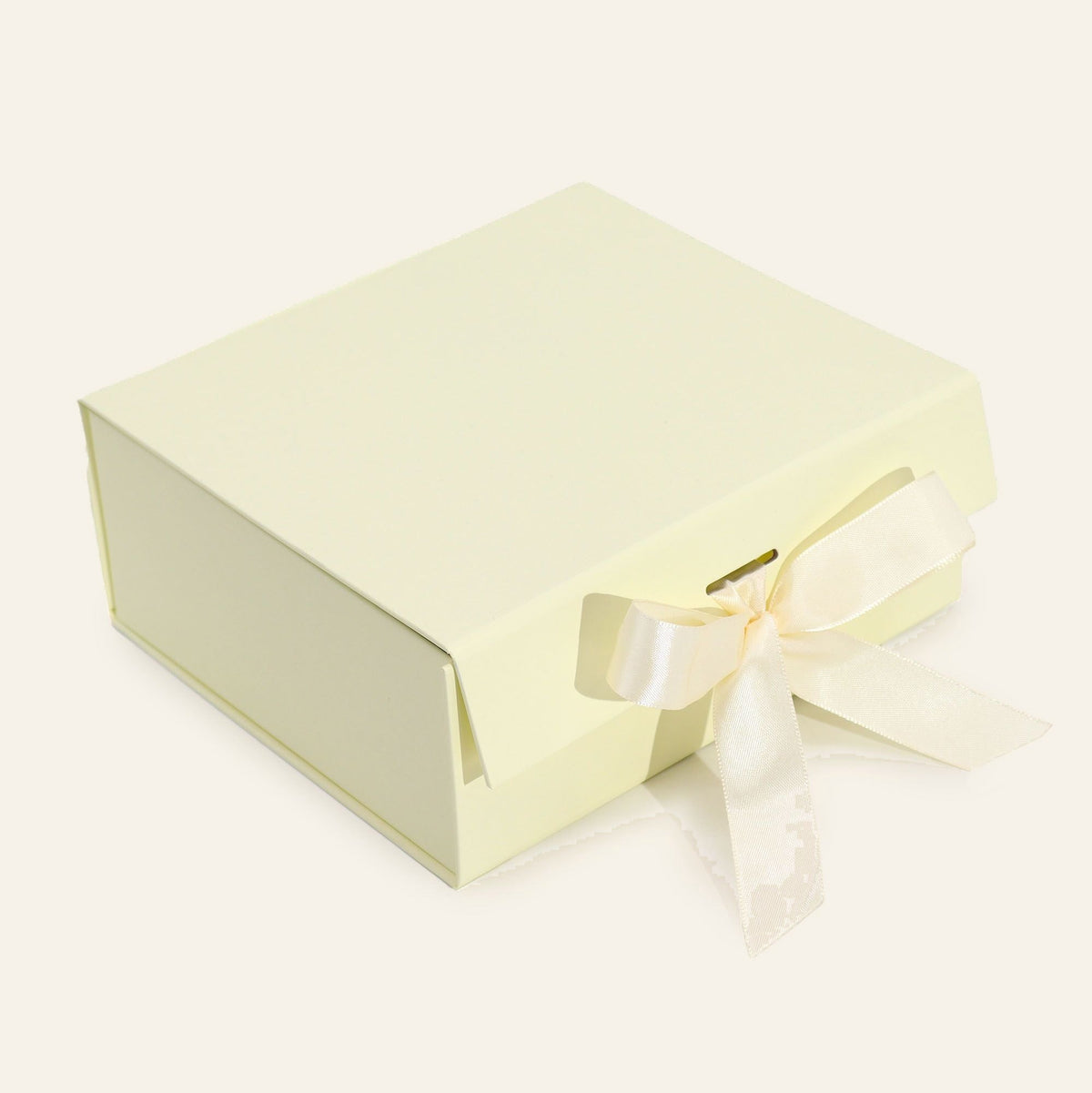 Ivory gift box, medium, folded up with the lid closed and a cream ribbon tied through it